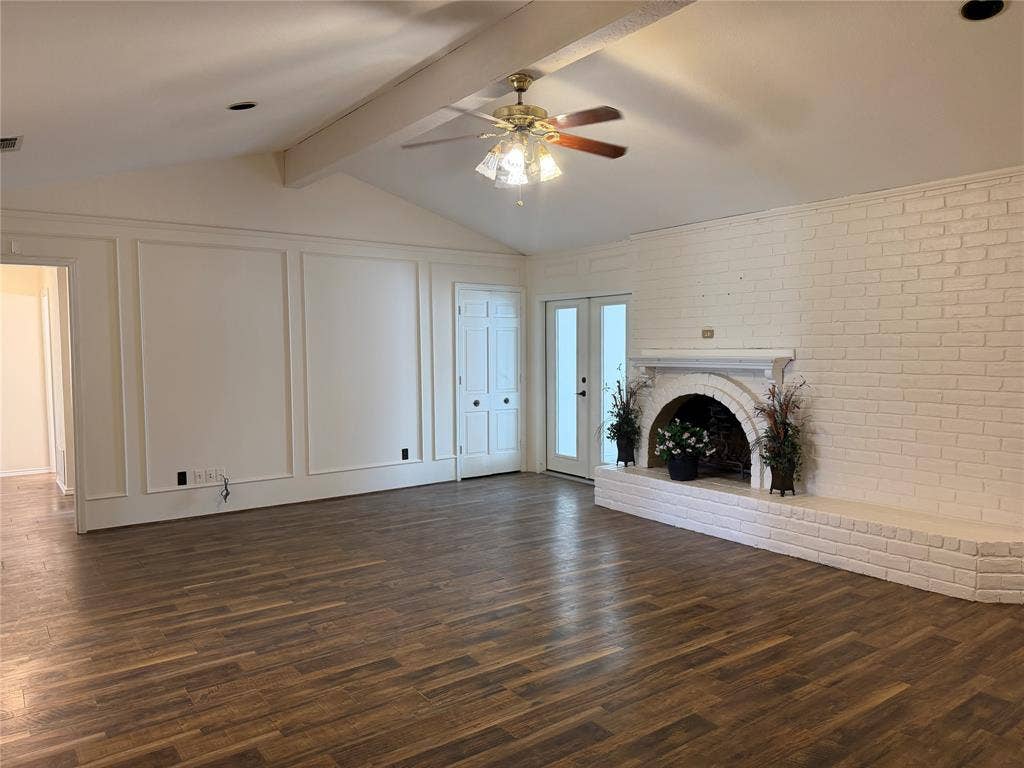 2408 Skiles Drive, Plano, TX 75075 Vaulted ceiling with exposed beam, wood-finish flooring, white brick fireplace with hearth, white paneled wall, and double glass-paneled doors