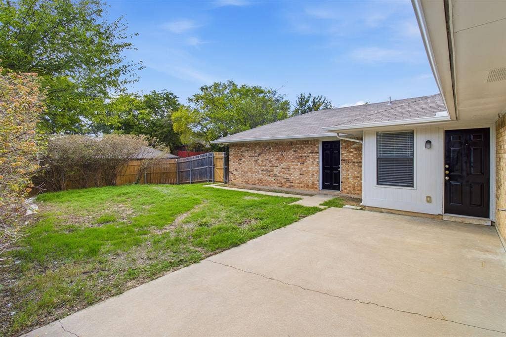 438 Blueridge Drive, Duncanville, TX 75137 Rear exterior featuring a concrete patio, brick and siding facade, two dark-toned entry doors, and a fenced yard with mature landscaping