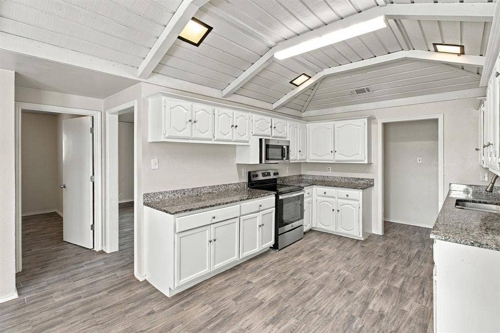438 Blueridge Drive, Duncanville, TX 75137 Kitchen featuring vaulted tongue-and-groove ceilings, white cabinetry, stone-finish countertops, stainless steel appliances, and wood-finish flooring