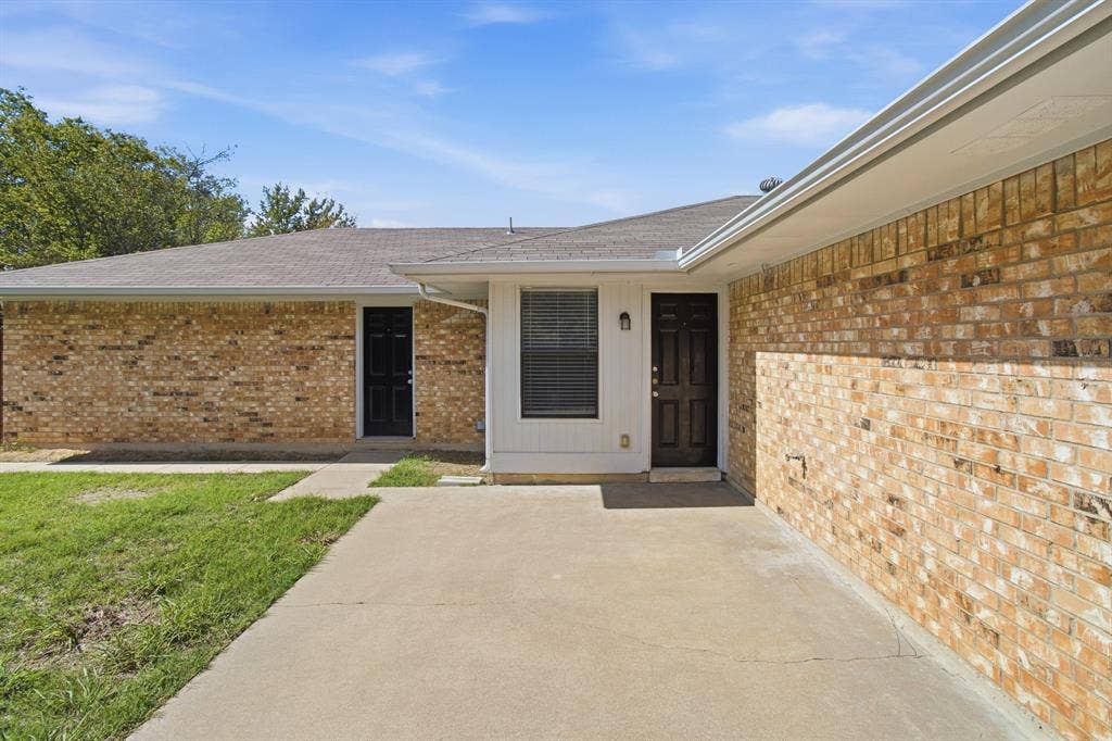 438 Blueridge Drive, Duncanville, TX 75137 Single-story exterior featuring multi-toned brick siding, a neutral-toned shingle roof, two solid-panel entry doors, and a concrete patio