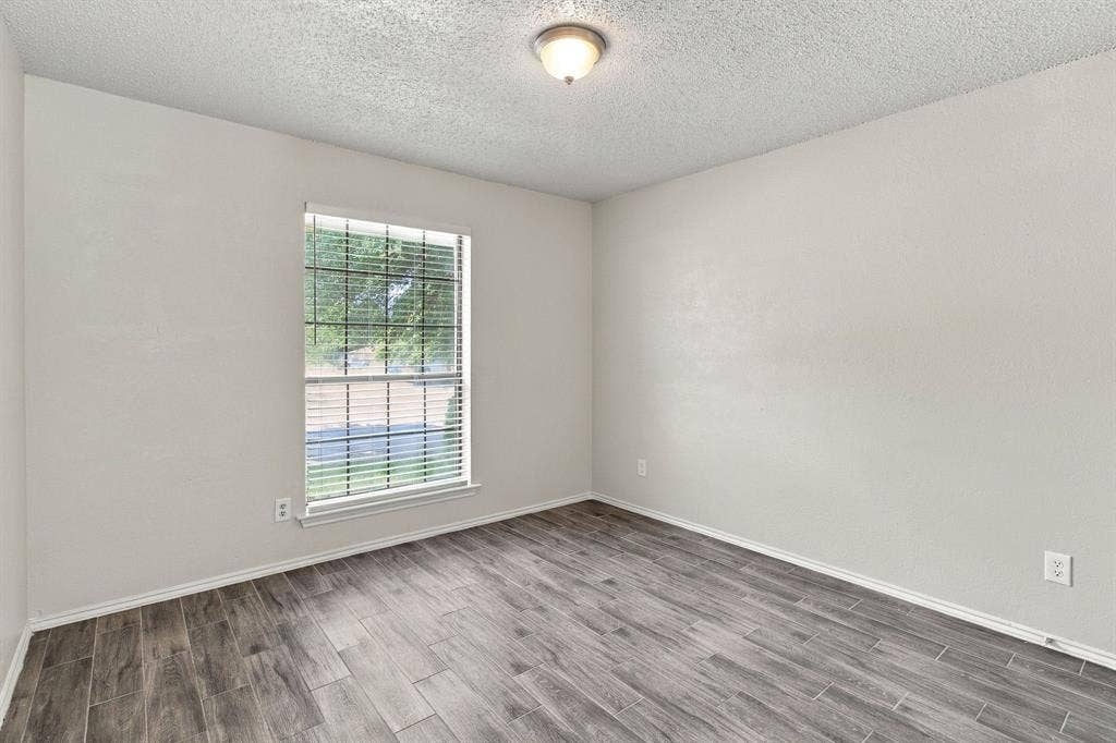 438 Blueridge Drive, Duncanville, TX 75137 Neutral-toned walls, wood-finish tile flooring, a large window with horizontal blinds, and a central flush-mount ceiling light fixture