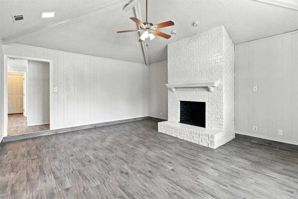 438 Blueridge Drive, Duncanville, TX 75137 Vaulted ceiling with an integrated ceiling fan, white-painted brick fireplace with a decorative mantel, and wood-finish flooring