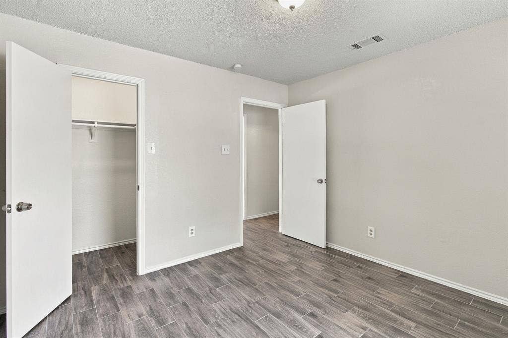 438 Blueridge Drive, Duncanville, TX 75137 Room featuring neutral wall paint, wood-finish flooring, two interior doors, and a built-in closet with integrated shelving