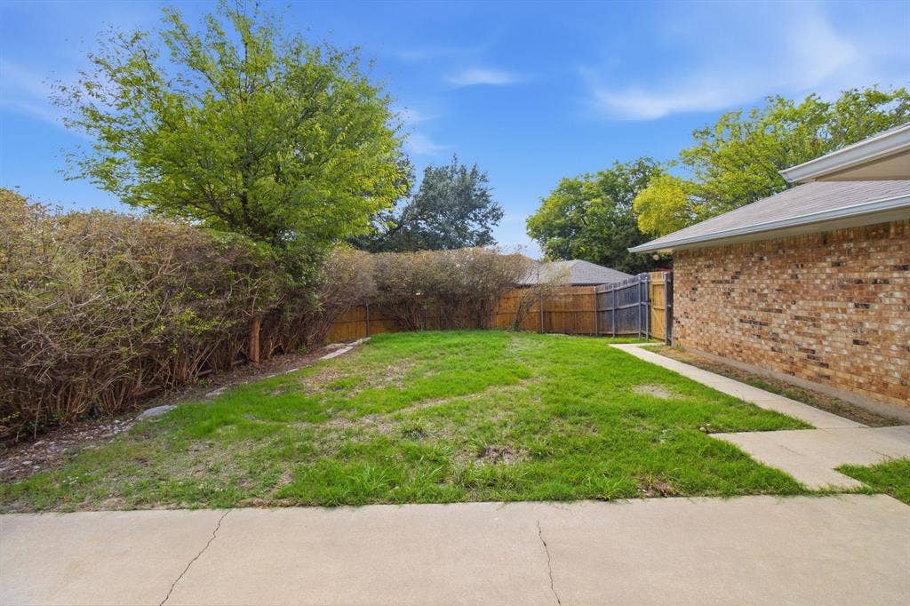 438 Blueridge Drive, Duncanville, TX 75137 Fenced backyard featuring a brick exterior wall, concrete patio, grass lawn, and mature perimeter hedging