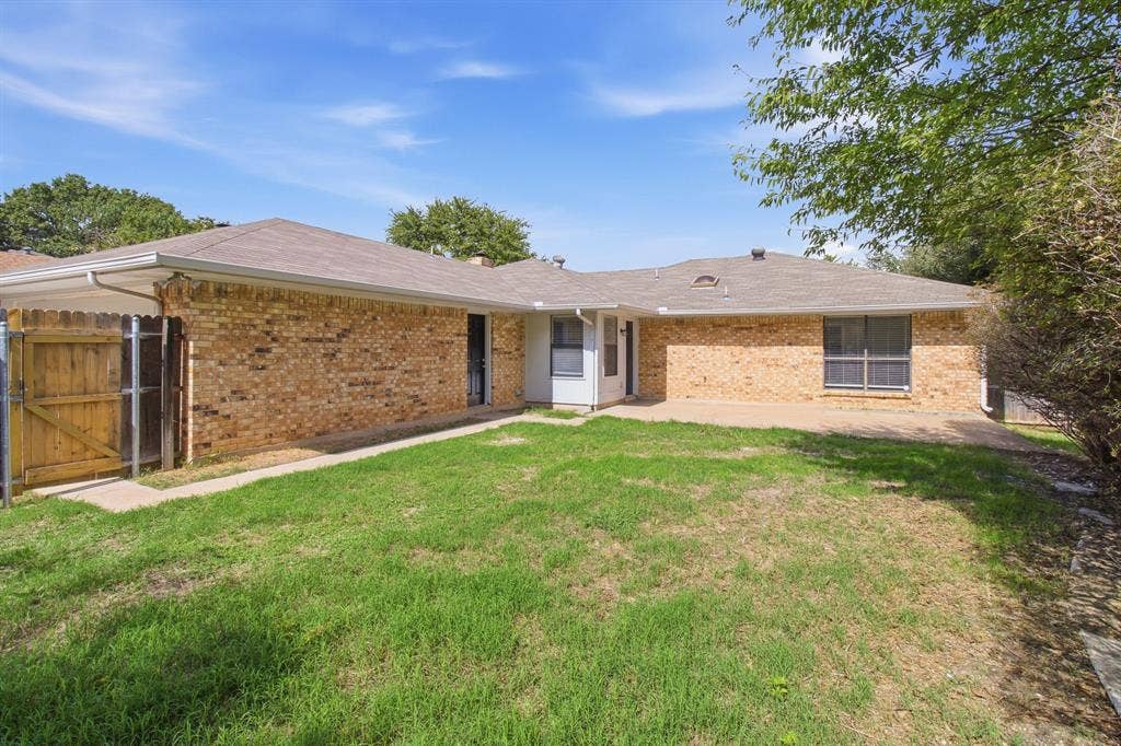 438 Blueridge Drive, Duncanville, TX 75137 Rear exterior featuring a brick facade, concrete patio, wood privacy fencing, and a grass lawn