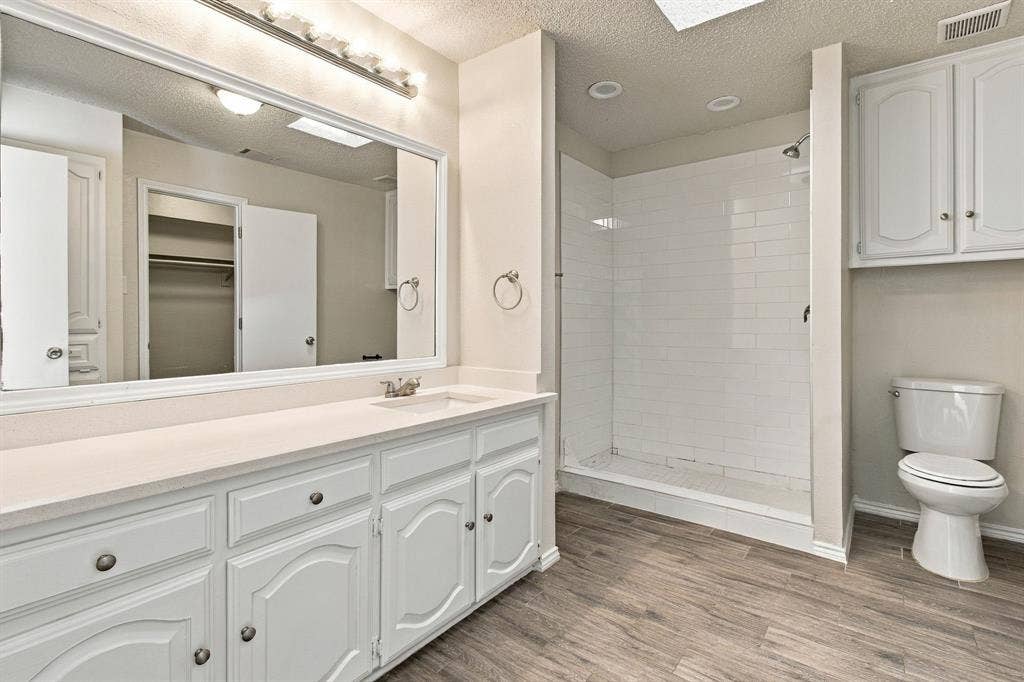 438 Blueridge Drive, Duncanville, TX 75137 Bathroom featuring a vanity with a solid-surface countertop, white cabinetry, subway-tiled walk-in shower, wood-finish flooring, and wall-mounted cabinetry