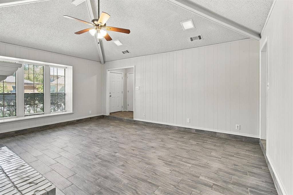 438 Blueridge Drive, Duncanville, TX 75137 Vaulted ceiling featuring a central wood-finish ceiling fan, vertical wall paneling, wood-finish flooring, and multiple window panes