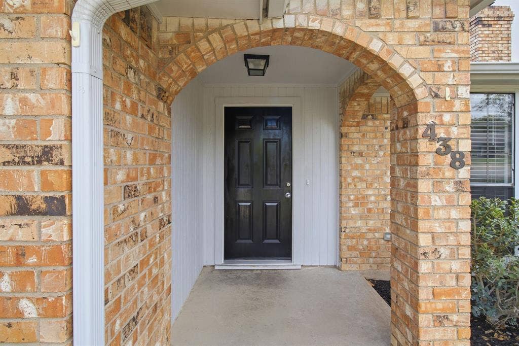 438 Blueridge Drive, Duncanville, TX 75137 Covered entryway featuring a brick facade, arched masonry detailing, a solid-panel door, and an overhead flush-mount light fixture