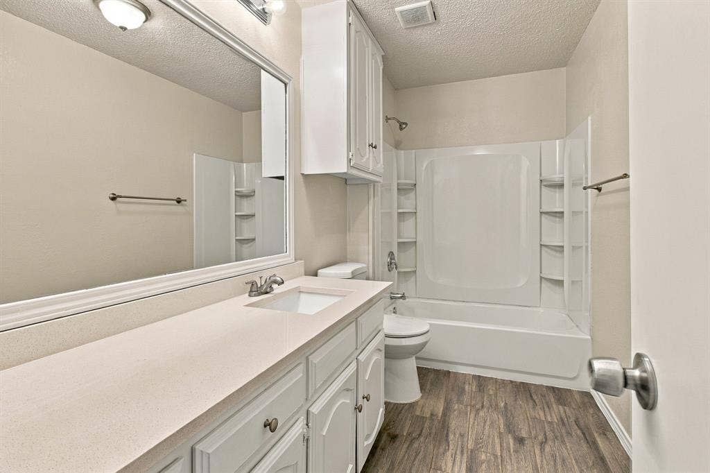 438 Blueridge Drive, Duncanville, TX 75137 Bathroom featuring a single-sink vanity with a solid-surface countertop, full-width mirror, wood-finish flooring, and a tub-shower combination with integrated shelving