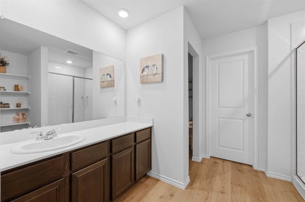 6535 Sand Dune Way, Princeton, TX 75407 Bathroom featuring a dark wood-finish vanity, solid surface countertop with an integrated oval sink, full-width wall mirror, wood-finish flooring, and built-in shelving
