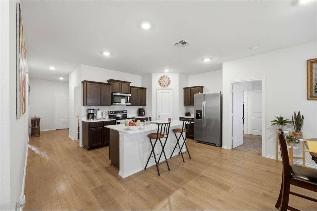 6535 Sand Dune Way, Princeton, TX 75407 Kitchen featuring dark-toned cabinetry, stainless steel appliances, a central island with white stone-finish countertop, and wood-finish flooring