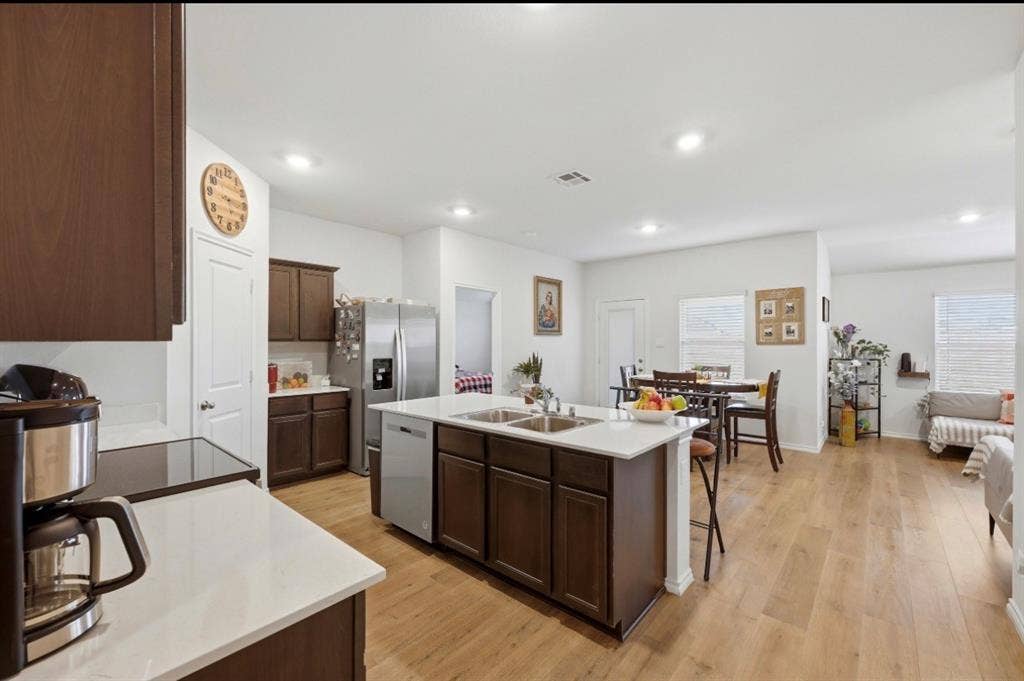 6535 Sand Dune Way, Princeton, TX 75407 Kitchen featuring wood-finish cabinetry, white countertops, a center island with a dual-basin sink, stainless steel appliances, and wood-finish flooring