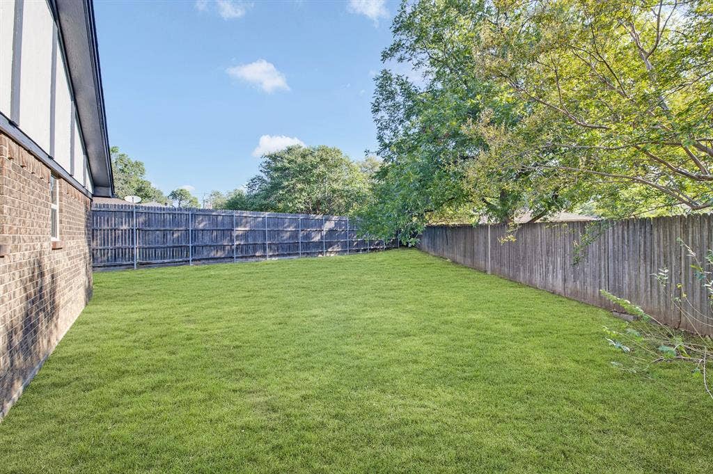 912 Shell Court, Bedford, TX 76022 Expansive fenced backyard featuring a manicured lawn, mature trees, and a brick exterior