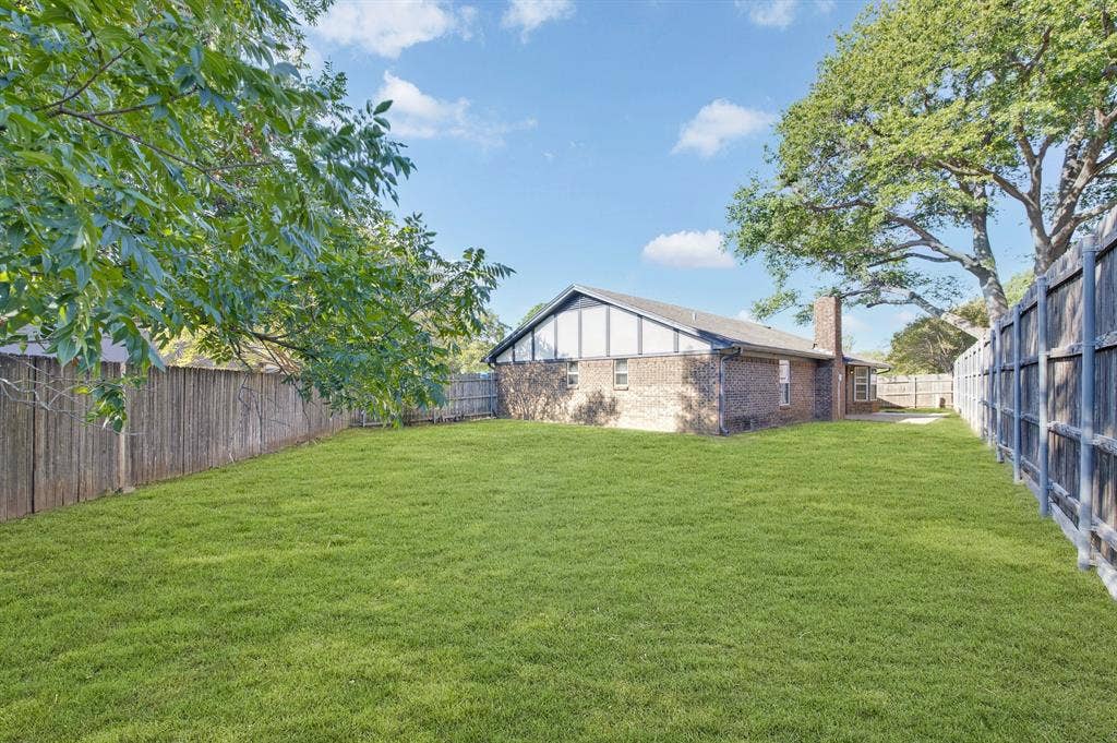 912 Shell Court, Bedford, TX 76022 Expansive backyard featuring a manicured lawn, full perimeter fencing, mature trees, and a brick exterior with a pitched roof