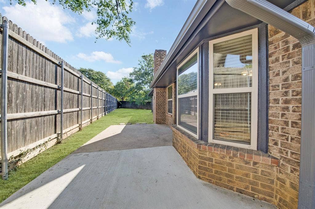 912 Shell Court, Bedford, TX 76022 Brick exterior with white-framed windows, concrete patio, and fenced yard