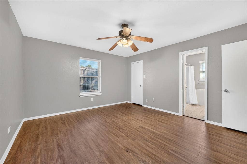 912 Shell Court, Bedford, TX 76022 Spacious bedroom featuring warm wood-finish flooring, neutral gray walls, ceiling fan with integrated lighting, and abundant natural light from large window