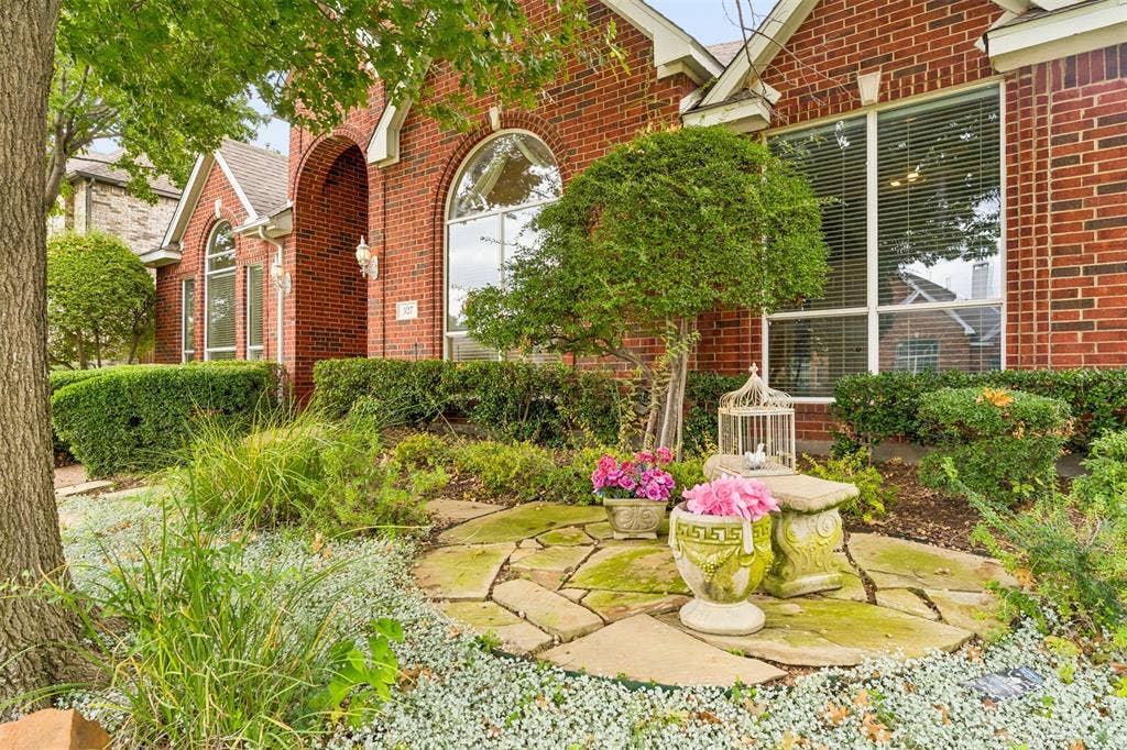 327 Hampton Court, Coppell, TX 75019 Brick exterior featuring an arched entryway, stone patio hardscaping, and large multi-pane windows