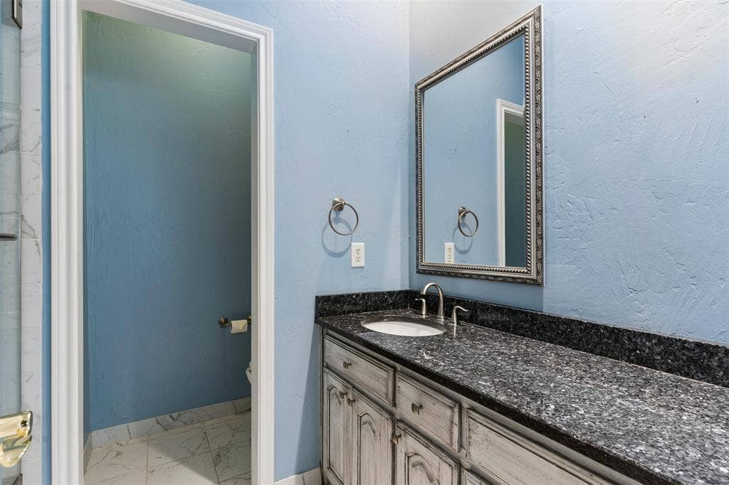 327 Hampton Court, Coppell, TX 75019 Custom cabinetry with a distressed finish, dark stone-top vanity, undermount sink, arched chrome faucet, and rectangular framed mirror