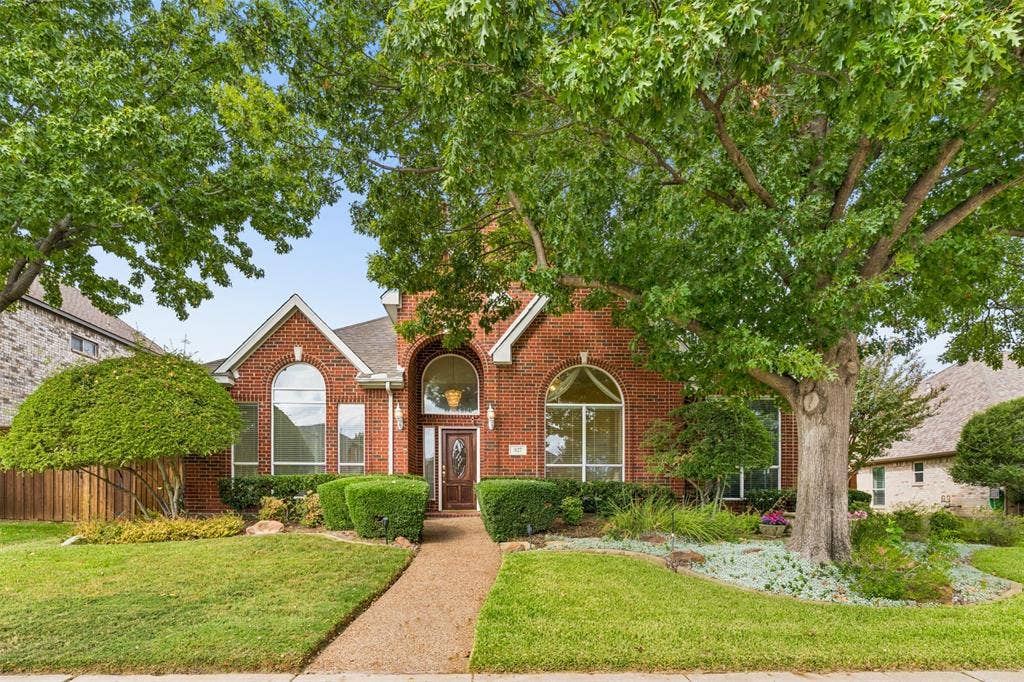 327 Hampton Court, Coppell, TX 75019 Red brick exterior featuring a steep-pitched roofline, an arched entryway with decorative glass door, and large multi-pane windows with arched transoms