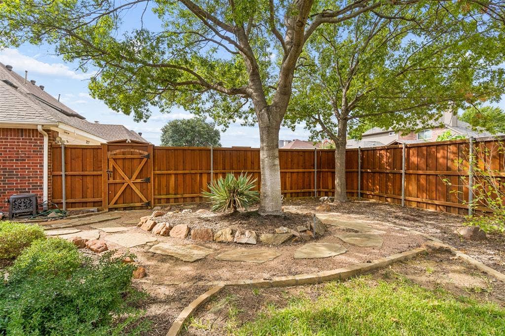 327 Hampton Court, Coppell, TX 75019 Backyard featuring a wood privacy fence, stone-bordered landscaping, mature trees, and natural stone hardscaping