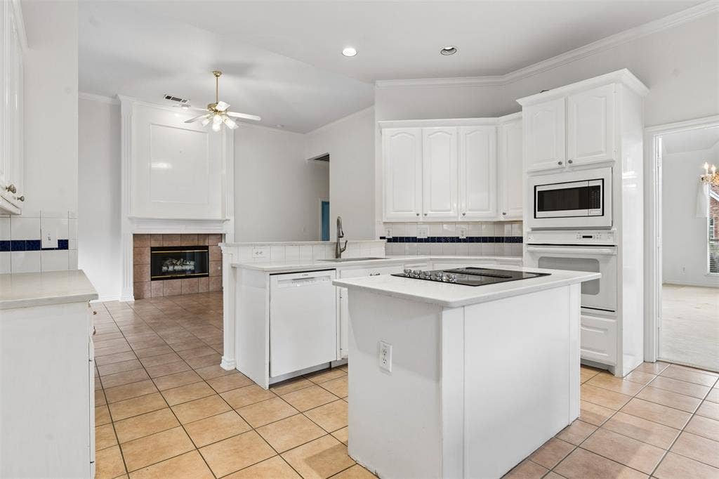 327 Hampton Court, Coppell, TX 75019 Kitchen featuring white cabinetry, center island with an integrated cooktop, built-in wall oven and microwave, ceramic tile flooring, and a fireplace with tile surround