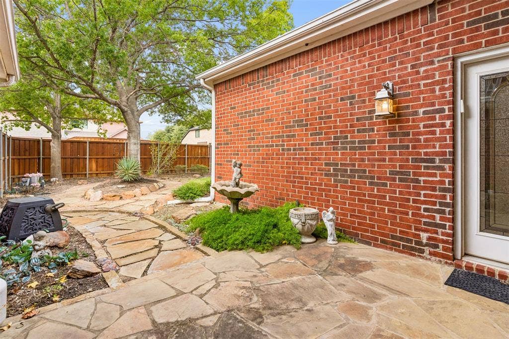 327 Hampton Court, Coppell, TX 75019 Exterior brick facade featuring a flagstone patio, winding natural stone pathway, and wood privacy fencing