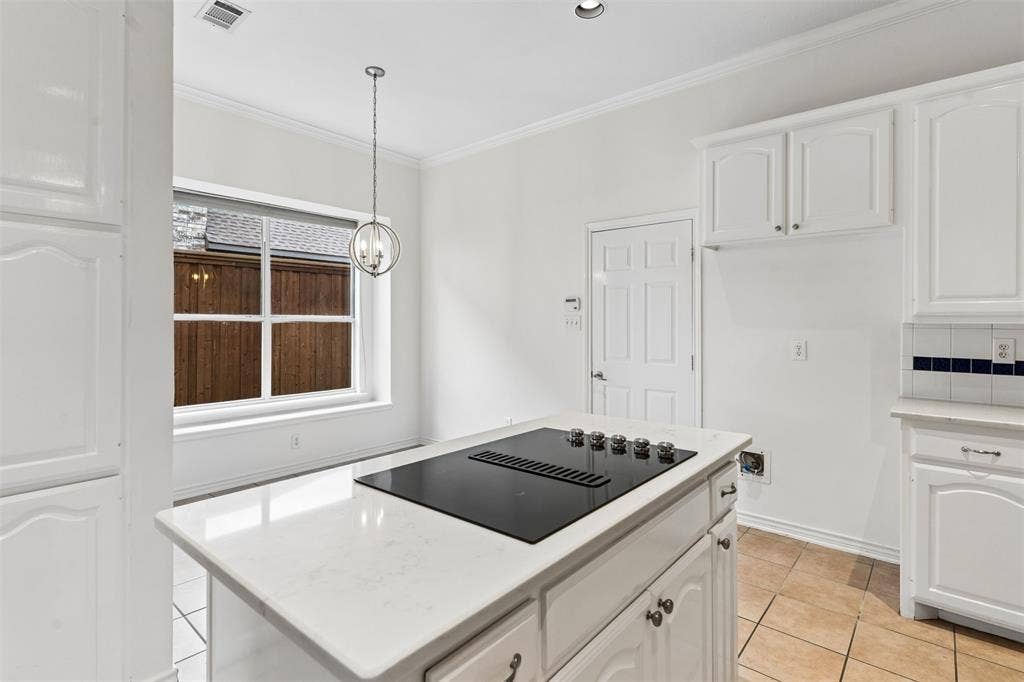 327 Hampton Court, Coppell, TX 75019 Kitchen island with a light-toned solid surface countertop and built-in electric cooktop, white cabinetry, tile flooring, and a multi-light pendant fixture