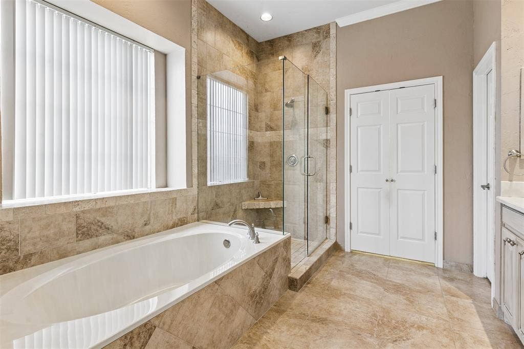 327 Hampton Court, Coppell, TX 75019 Oval soaking tub with stone tile surround, frameless glass-enclosed shower, neutral-tone wall finishes, and double-door entry