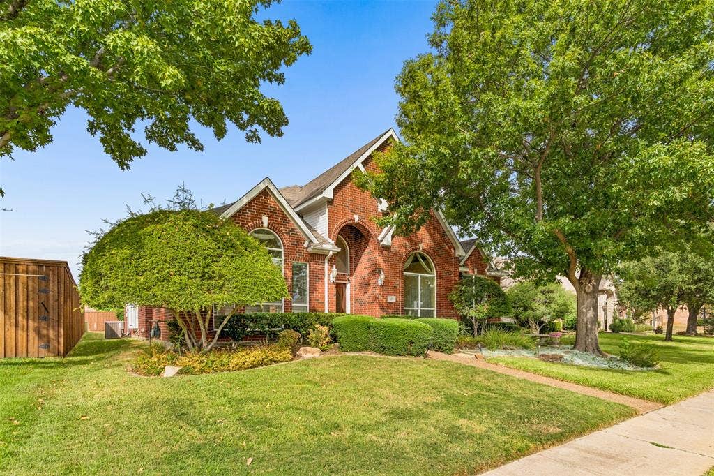 327 Hampton Court, Coppell, TX 75019 Brick exterior featuring an arched entryway, steep roof gables, and large arched windows, set on a landscaped lot with mature trees