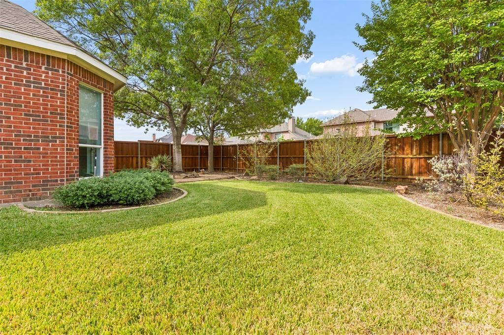 327 Hampton Court, Coppell, TX 75019 Backyard featuring a red brick exterior, manicured lawn, established shade trees, and a wooden perimeter fence