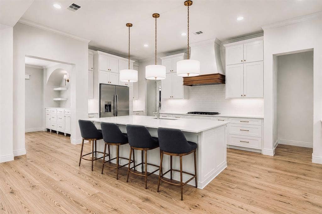6651 Pinehurst Drive, Granbury, TX 76049 Gourmet kitchen featuring a substantial island, wood-finish flooring, stainless steel appliances, white cabinetry, and pendant lighting