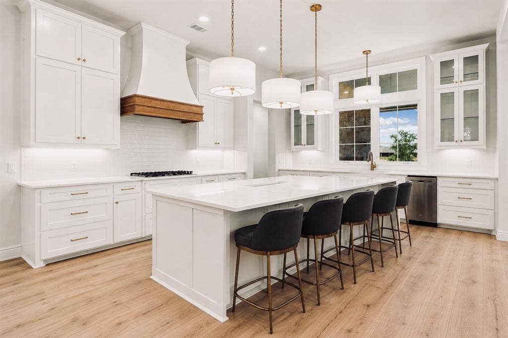 6651 Pinehurst Drive, Granbury, TX 76049 Spacious kitchen featuring an expansive island, white cabinetry, integrated stainless steel appliances, a wood-finish range hood, and wood-finish flooring
