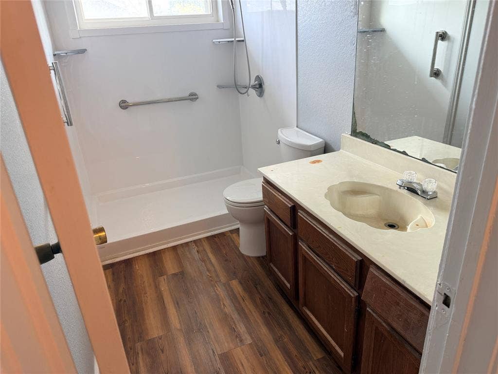 1644 Taylorcrest Drive, Dallas, TX 75253 Bathroom featuring wood-finish flooring, a vanity with a light-colored countertop and integrated sink, and a shower with a grab bar