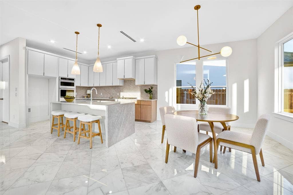 Kitchen featuring stone-topped island with waterfall edge, white cabinetry, integrated stainless steel double wall oven, polished tile flooring, and multi-arm brass light fixture
