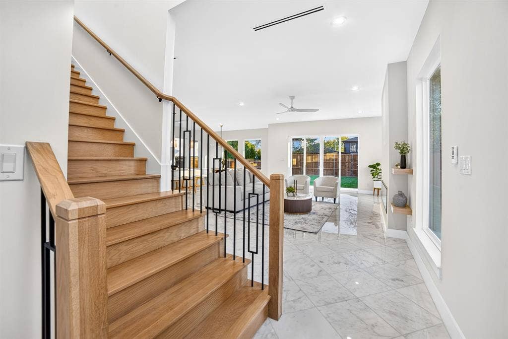 Staircase with wood treads, handrail, and geometric black metal balusters, complemented by light-toned stone-finish tile flooring, recessed lighting, and wall-mounted floating shelving