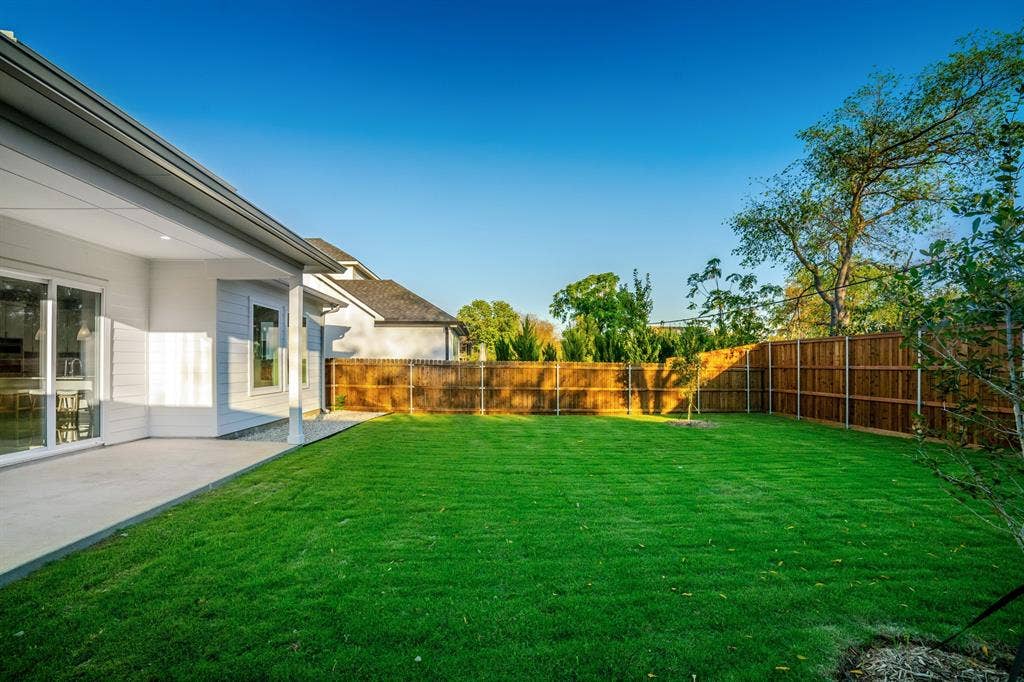 Covered concrete patio, fenced backyard, and manicured lawn