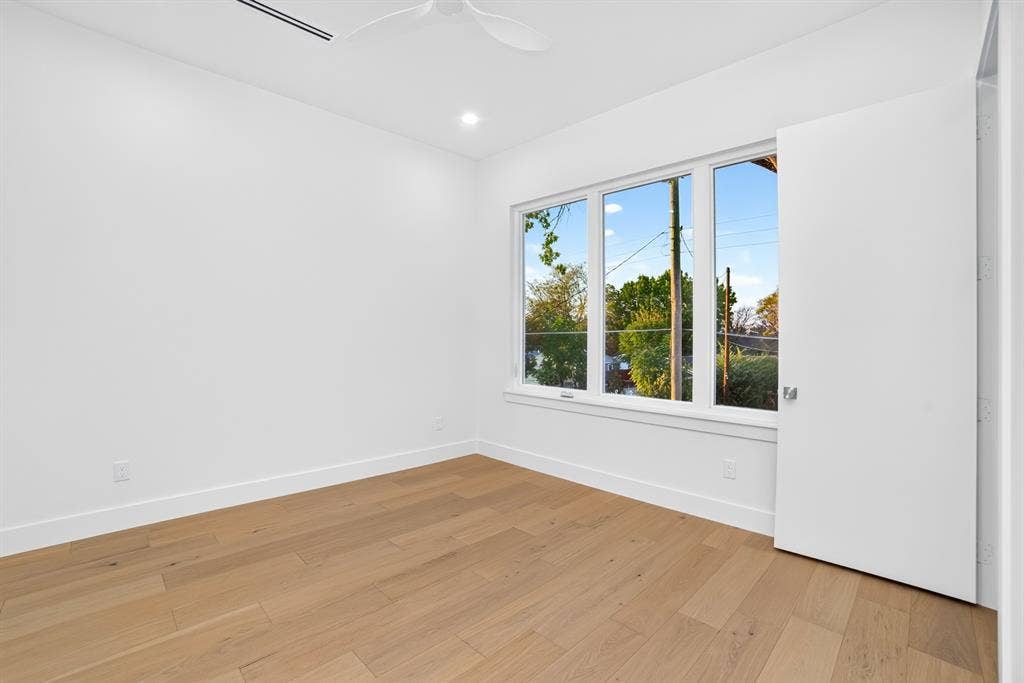 Neutral interior featuring wood-finish flooring, white walls, large triple-pane windows, and a ceiling-mounted fan