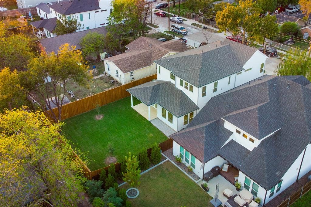 Two-story residence featuring a multi-pitched shingled roof, white exterior siding, a private fenced yard, a covered rear patio, and hardscaped outdoor areas