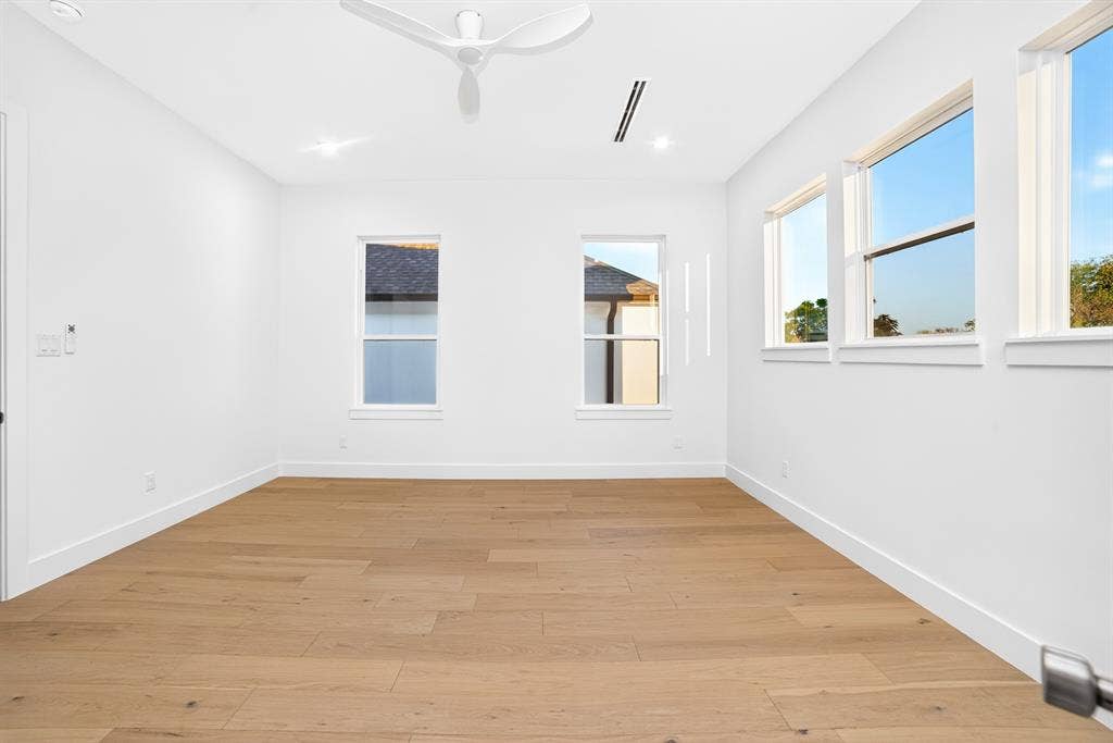Interior space featuring wood-finish flooring, white walls, multiple windows, a modern white ceiling fan, and recessed lighting