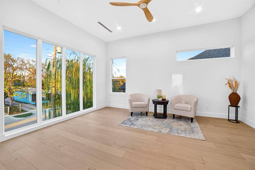 High-ceiling interior featuring light wood-finish flooring, floor-to-ceiling windows, recessed lighting, and a modern wooden ceiling fan