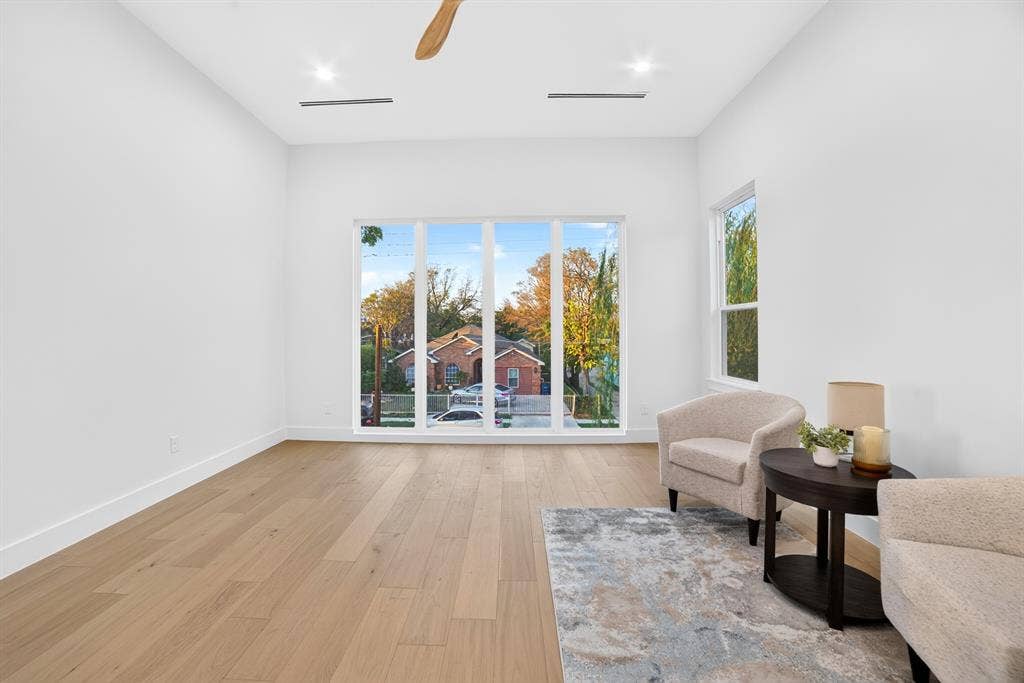 High-ceilinged room featuring wood-finish flooring, recessed lighting, a ceiling fan, and large picture windows
