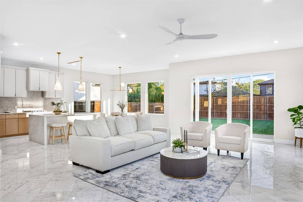 Open-concept interior featuring large-format tile flooring, a central kitchen island with waterfall-edge stone counters, multi-pendant lighting, and floor-to-ceiling sliding glass doors