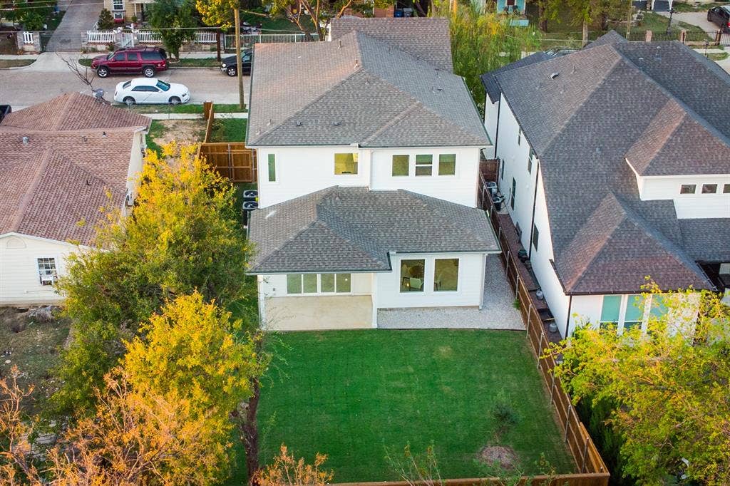Two-story exterior featuring a light-toned smooth facade, dark asphalt shingle roofing, a ground-level concrete patio, and a fully fenced private rear lawn
