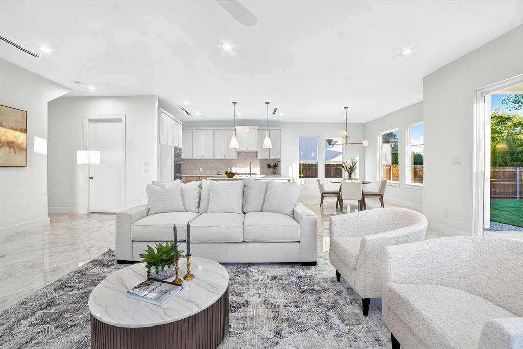 Open-concept interior featuring light-toned stone-finish tile flooring, recessed ceiling lighting, a contemporary kitchen with white cabinetry, and large windows providing natural light