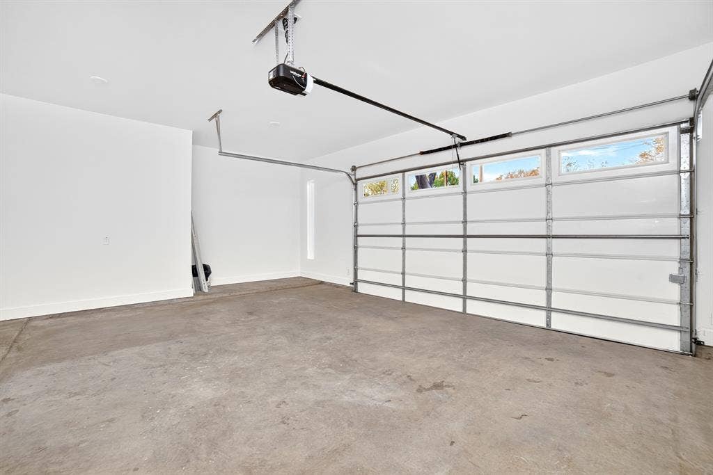 Finished garage featuring concrete flooring, white walls, automated door opener, and a panelled garage door with horizontal glass windows