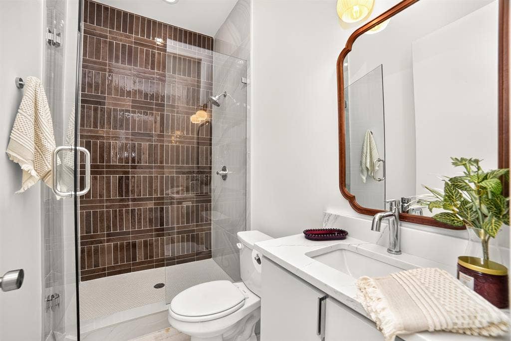 Bathroom featuring a glass-enclosed walk-in shower with vertical tile surround, white vanity with stone-style countertop, integrated sink, and wall-mounted lighting