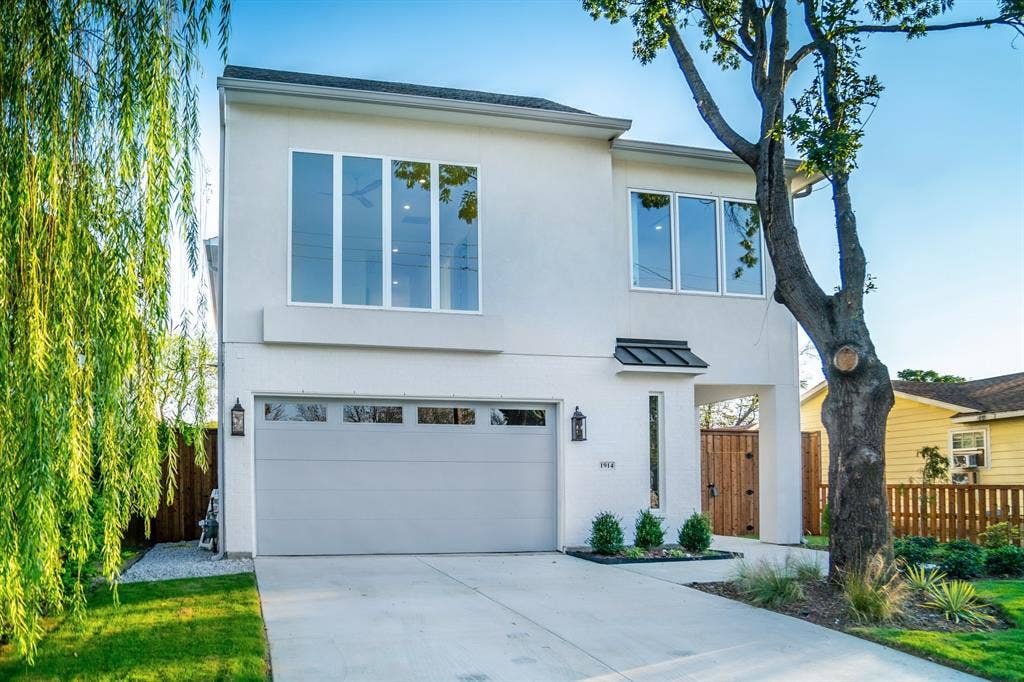 Two-story exterior featuring a smooth stucco finish, large-pane windows, a recessed entryway with a metal awning, and a dedicated concrete driveway