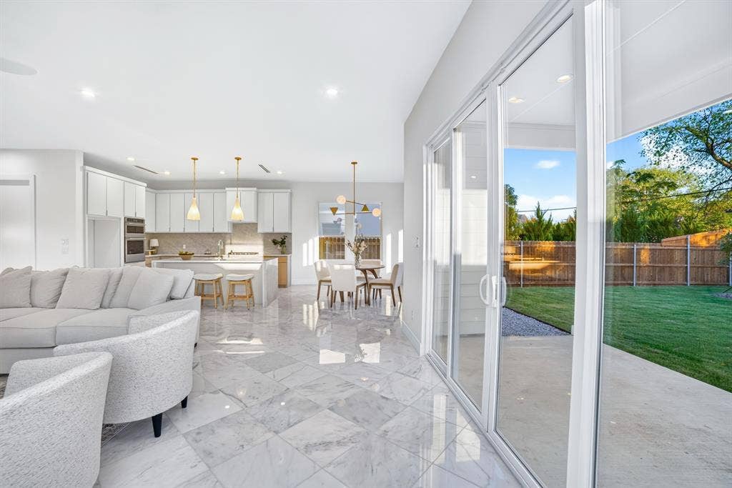 Open-concept interior featuring large-format tile flooring, white cabinetry, integrated stainless steel double wall ovens, recessed lighting, and multi-panel sliding glass doors