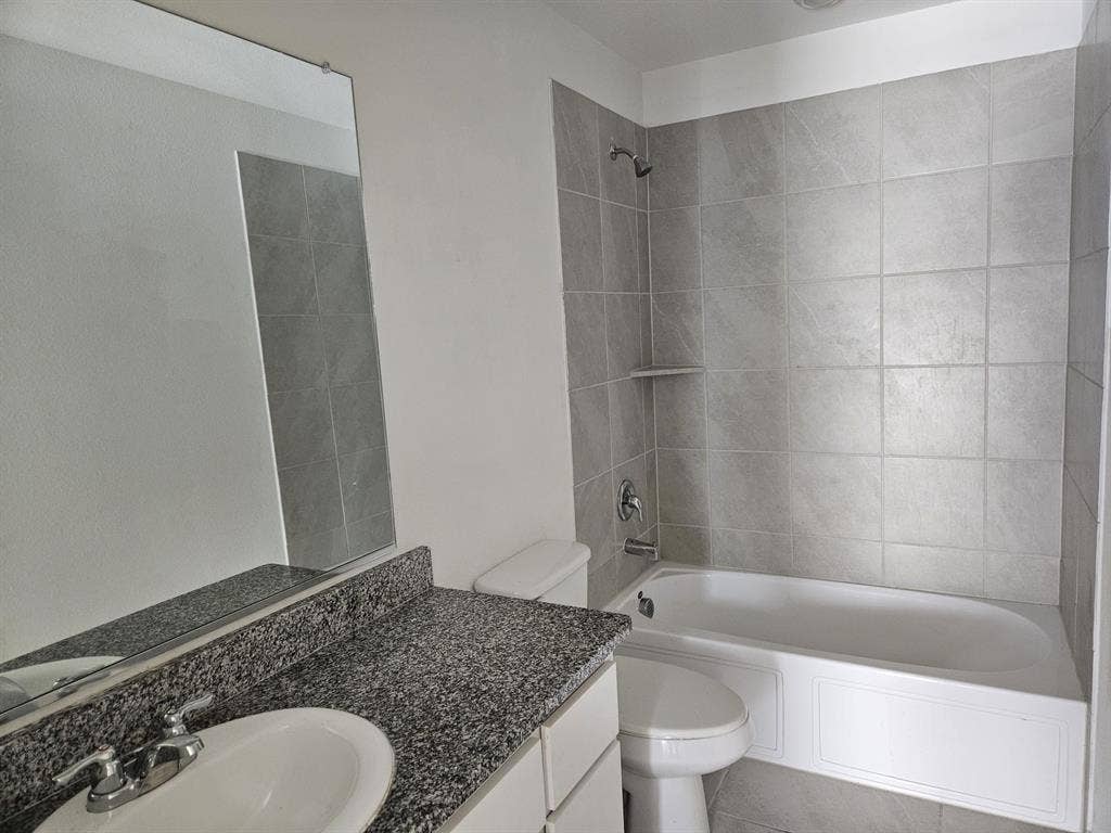 3338 Beckwith Way, Crandall, TX 75114 Bathroom featuring a white vanity with a speckled countertop, an integrated sink, a rectangular mirror, and a shower-over-tub with light gray tile surround