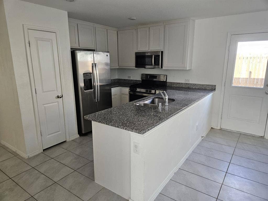 3338 Beckwith Way, Crandall, TX 75114 White upper and lower cabinetry, stainless steel appliances, granite countertops, tile flooring, and a glass-paned exterior door
